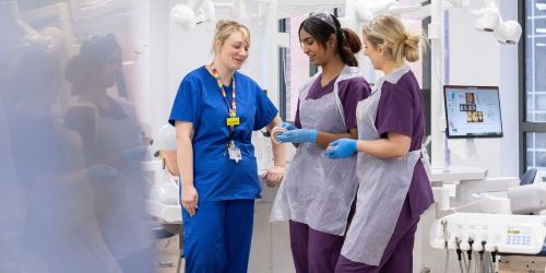 A dental student watching a tutor work on a patient